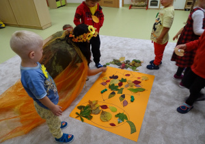 Dzieci ozdabiają krasnala liśćmi.